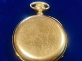an antique gold pocket watch on a blue velvet surface