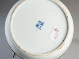 a white plate with a blue flower on it sitting on a stand