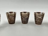 six silver shot glasses with designs on them on a white surface