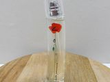 a small glass bottle with a red flower in it on a wooden table