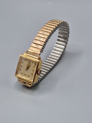 une image représentant une montre-bracelet dorée et argentée posée sur une surface grise