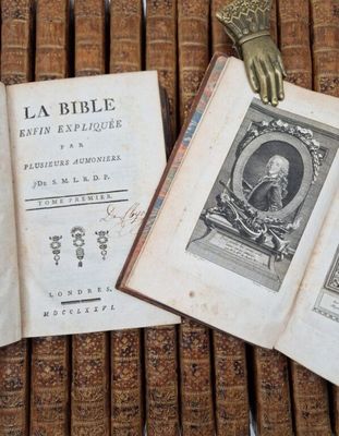 an old book with a statue of a hand on top of it next to a bunch of old books