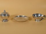 trois objets en argent posés sur une table, à côté d'un bol et d'une tasse