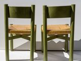 pair of green wooden chairs with woven seats against a white wall