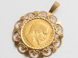 un gros plan d'une pièce d'or sertie dans un pendentif, posée sur une surface blanche