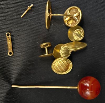 une paire de boutons de manchette en or et une boule rouge posée sur un tissu noir
