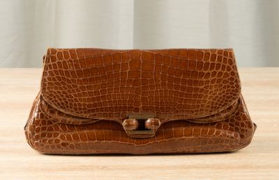 crocodile skin purse on a wooden table with a curtain in the background