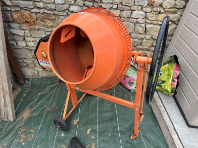 an orange cement mixer sitting on the ground next to a brick wall