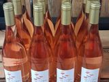 Six bouteilles de vin rosé sont alignées sur une table en bois