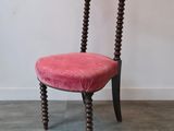 une chaise rose posée sur un parquet, près d'un mur blanc