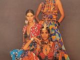 three women in colorful dresses posing for a photo in front of a gray background