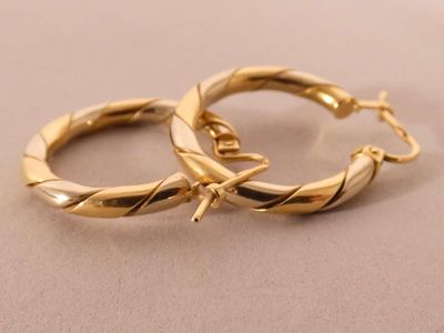 two gold hoop earrings on a beige surface