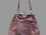 sac à main en cuir marron avec des anses cloutées sur fond gris