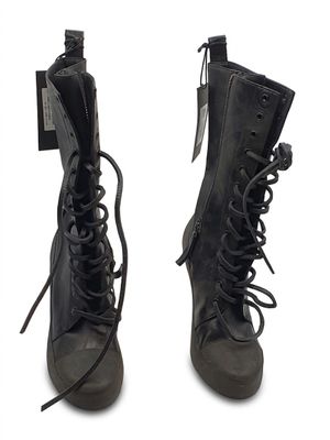 une paire de bottes en cuir noir à lacets, avec une étiquette sur fond blanc