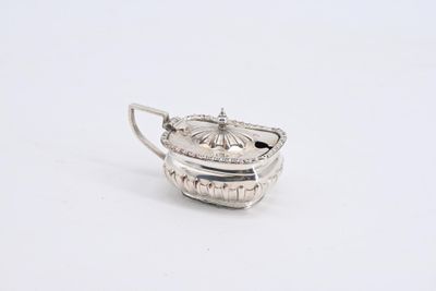 une théière ancienne en argent posée sur une surface blanche, munie d'une anse