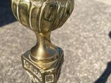 a gold vase sitting on a sidewalk with a shadow of a person in the background