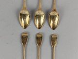 six gold spoons and two silver spoons on a white surface