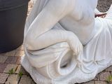 a statue of a woman reading a book on the ground