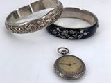 two silver bracelets and a pocket watch on a table