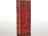 an old red book sitting on top of a table next to a white wall