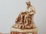 a beer mug with a statue of a man sitting on top of it