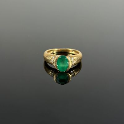 an emerald and diamond ring on a reflective surface