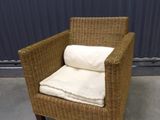 a wicker chair with pillows on it in front of a blue wall