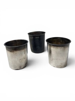 three metal cups are lined up in a row on a white surface