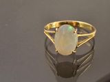 yellow gold ring with a white opal stone on a reflective surface