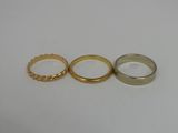 three gold wedding rings on a white surface