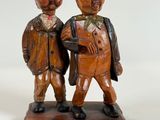 wooden figurines of two men with hats and canes on a white background