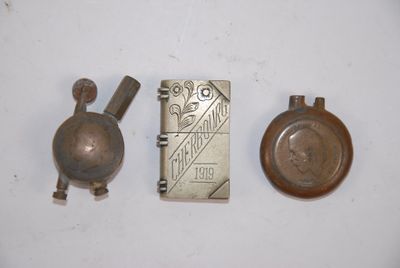trois briquets anciens en laiton et un étui à briquets posés sur une surface blanche