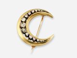une photo d'une broche en forme de croissant en or, sertie de diamants noirs et blancs