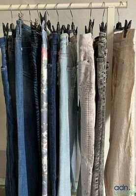 plusieurs paires de jeans suspendues à un portant devant un miroir