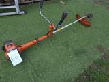 une débroussailleuse orange posée au milieu d'un champ recouvert d'herbe