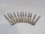 six silverplated knives are lined up on a white surface