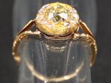 une image représentant une bague en or sertie d'un diamant jaune, posée sur un morceau de verre transparent