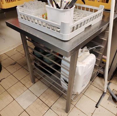 une table en métal sur laquelle est posé un panier contenant des ustensiles