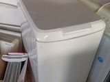 une machine à laver blanche posée par terre à côté d’une pile de cartons