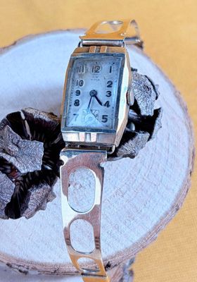 a silver watch sitting on top of a piece of wood