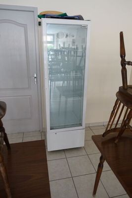 un petit réfrigérateur dans un coin d'une pièce où se trouve une chaise en bois