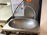 un lavabo dans des toilettes publiques, avec une affiche accrochée au mur