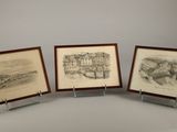 trois dessins encadrés représentant une ville et un bateau, posés sur une table