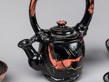 a black teapot with a red handle next to bowls and a tea pot