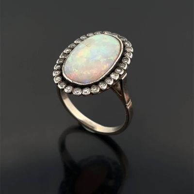 a white oplite and diamond ring on a black surface