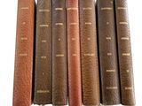 six old books are lined up in a row on a white surface