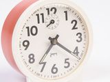 a small white clock with a red face on a white surface