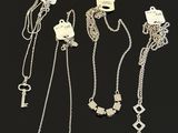 four different types of silver necklaces and a key on a black background