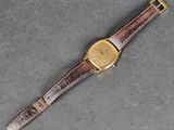 un gros plan d'une montre posée sur une surface grise, avec un bracelet marron