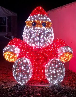 lighted santa claus sitting on a rock in front of a pink wall